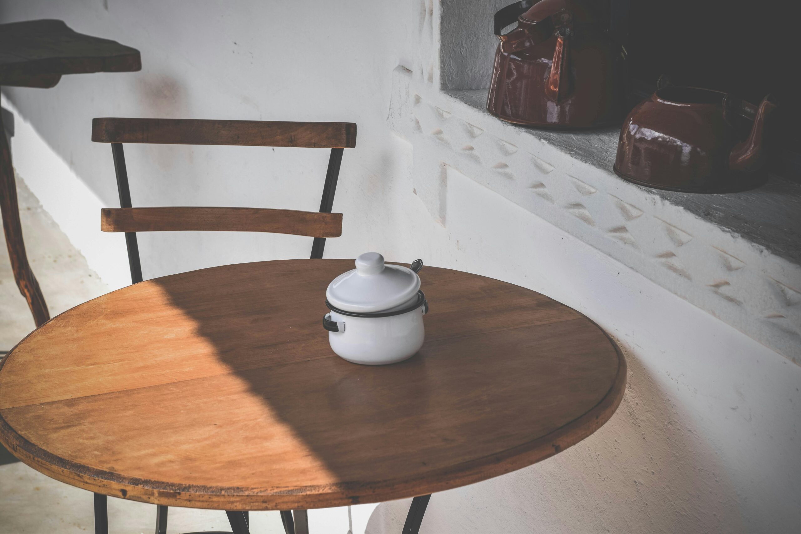 A cozy indoor scene featuring a rustic wooden table with a ceramic kettle and brown teapots on a ledge.