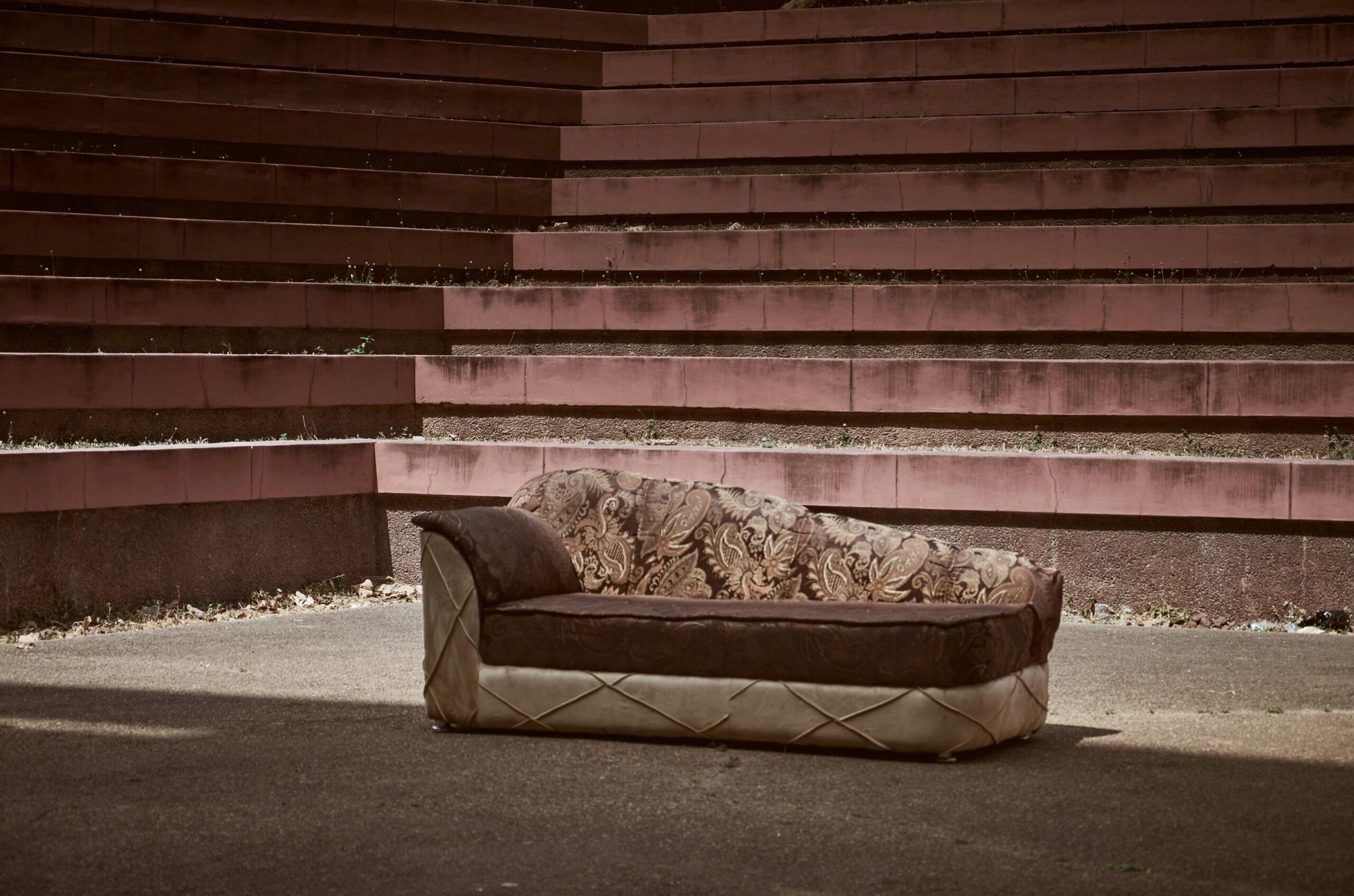 An abandoned ornate sofa amidst outdoor amphitheater steps in natural light.